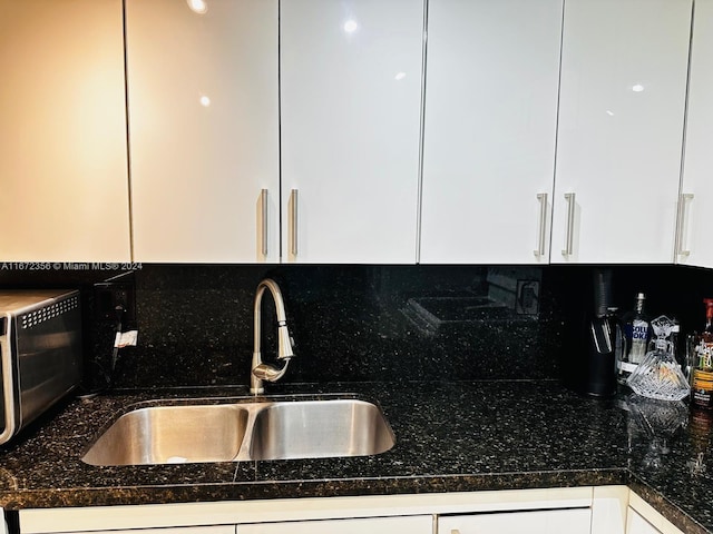 kitchen with dark stone counters, backsplash, white cabinets, and sink