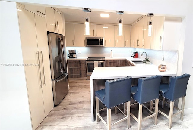 kitchen featuring light wood-type flooring, appliances with stainless steel finishes, a kitchen bar, hanging light fixtures, and sink