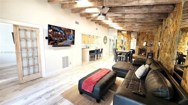 living room with a stone fireplace, sink, beamed ceiling, ceiling fan, and light hardwood / wood-style flooring