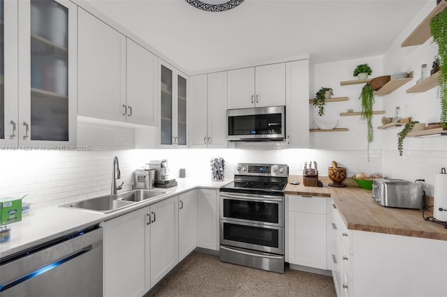 kitchen featuring open shelves, a sink, light speckled floor, appliances with stainless steel finishes, and butcher block counters