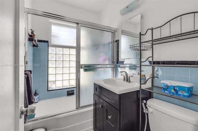 bathroom with vanity, bath / shower combo with glass door, wainscoting, tile walls, and toilet