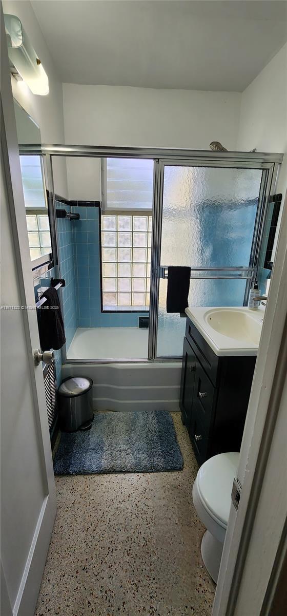 full bathroom with vanity, toilet, speckled floor, and enclosed tub / shower combo