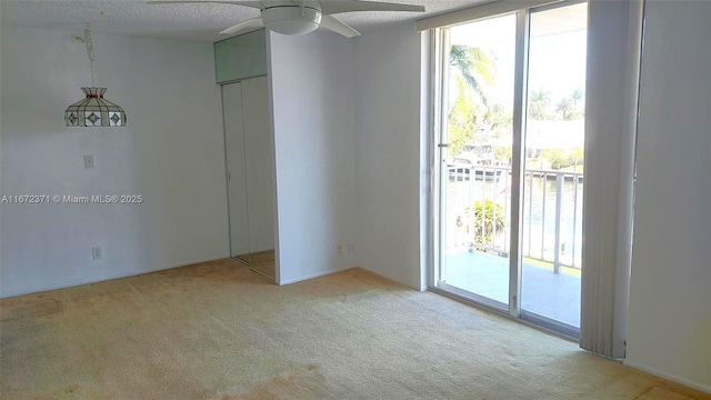 empty room featuring a textured ceiling, ceiling fan, floor to ceiling windows, and light carpet