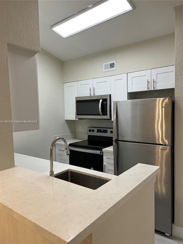 kitchen with stainless steel appliances, white cabinetry, kitchen peninsula, and sink