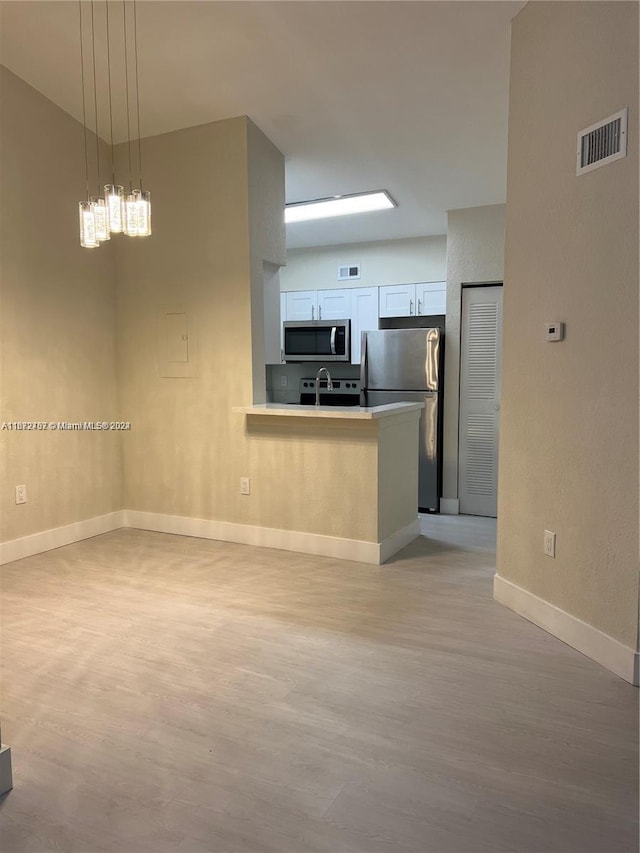 kitchen featuring stainless steel appliances, white cabinetry, hanging light fixtures, and light wood-type flooring