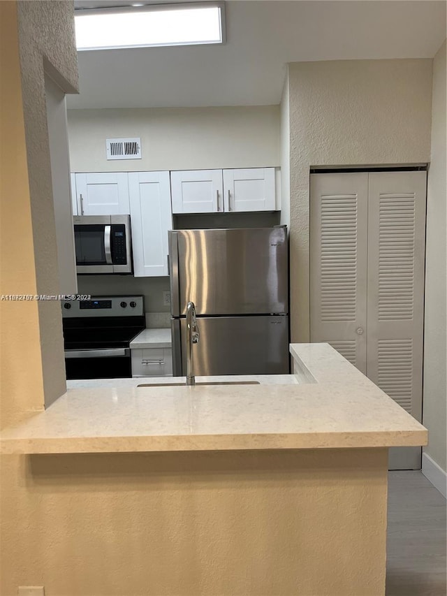 kitchen featuring sink, kitchen peninsula, white cabinetry, appliances with stainless steel finishes, and hardwood / wood-style floors