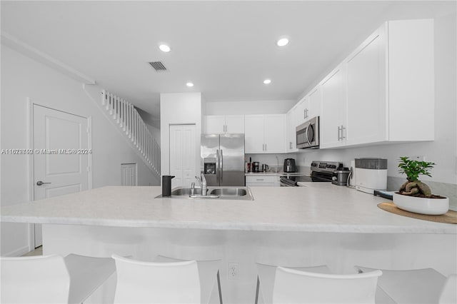 kitchen with a breakfast bar, kitchen peninsula, sink, appliances with stainless steel finishes, and white cabinetry