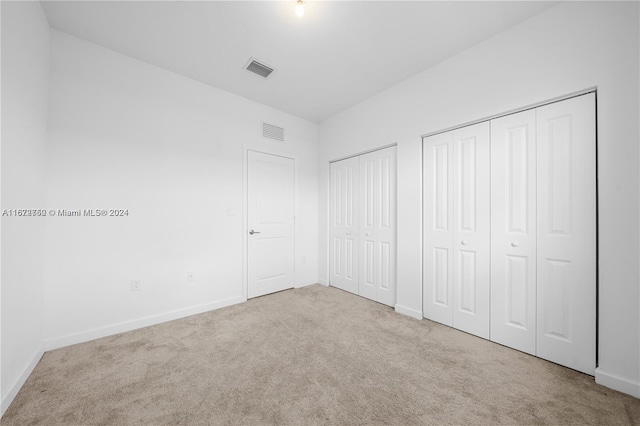 unfurnished bedroom with light carpet and two closets