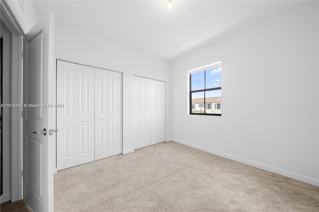 unfurnished bedroom featuring light colored carpet and two closets