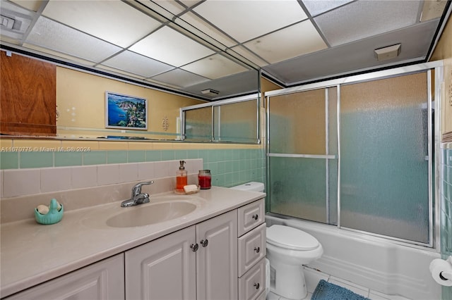 full bathroom featuring tile patterned floors, vanity, tile walls, enclosed tub / shower combo, and toilet