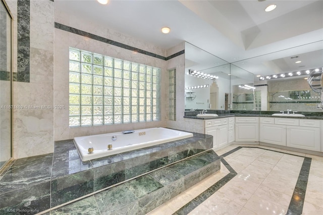 bathroom featuring a relaxing tiled tub, tile walls, and vanity