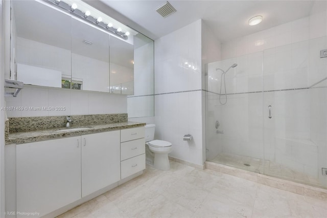 bathroom with an enclosed shower, vanity, tile walls, and toilet