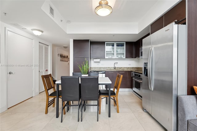 kitchen with a raised ceiling, dark brown cabinets, stainless steel appliances, and stone countertops