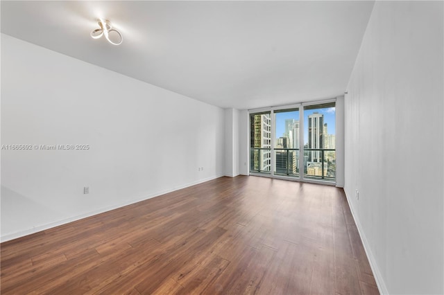 unfurnished room featuring expansive windows, a city view, dark wood-type flooring, and baseboards