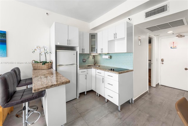 kitchen featuring white fridge, a breakfast bar area, kitchen peninsula, white cabinetry, and light stone counters