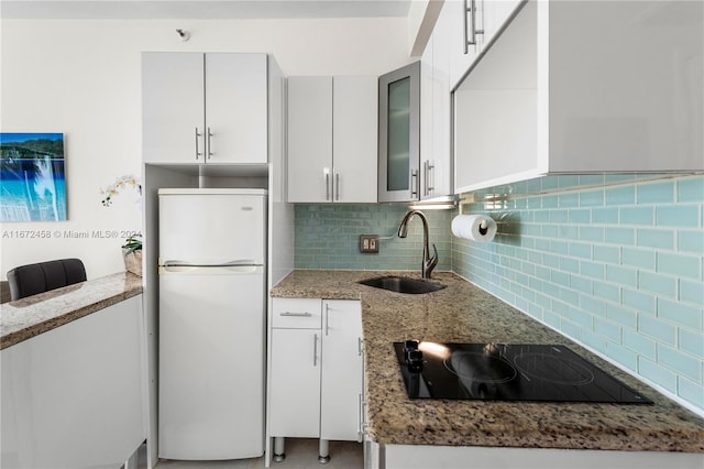 kitchen with dark stone countertops, sink, white refrigerator, and white cabinets