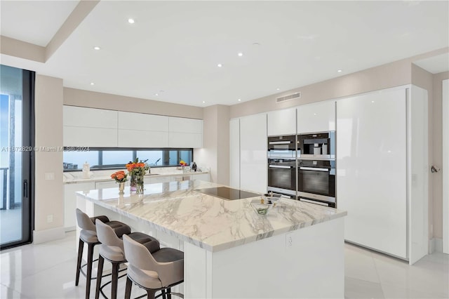 kitchen featuring white cabinetry, light stone countertops, a center island, black electric stovetop, and double oven