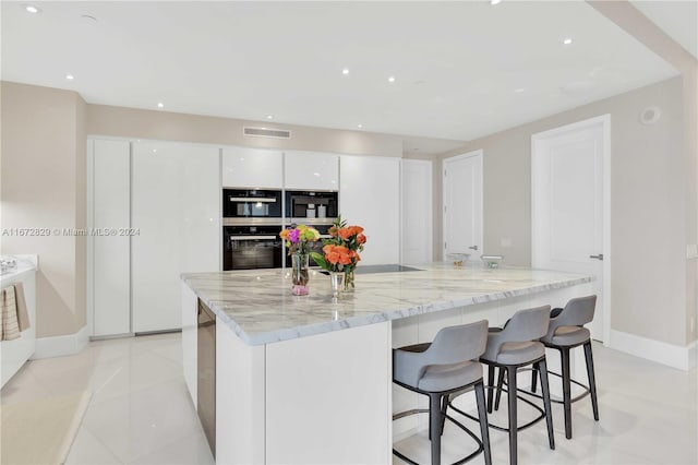 kitchen featuring white cabinets, baseboards, multiple ovens, light stone countertops, and a kitchen breakfast bar