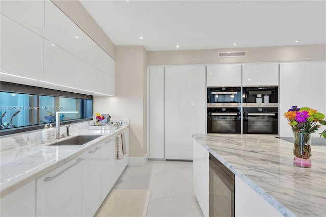 kitchen featuring light stone countertops, white cabinets, black double oven, and sink