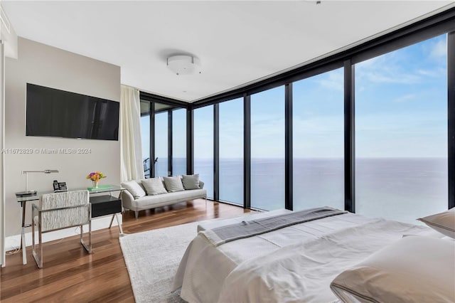 bedroom with expansive windows, hardwood / wood-style flooring, multiple windows, and a water view