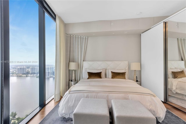 bedroom with light wood-type flooring, a water view, and a wall of windows