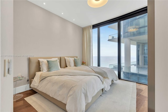 bedroom with wood finished floors, access to outside, expansive windows, a water view, and baseboards