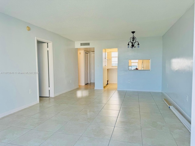 spare room featuring a textured ceiling, an inviting chandelier, and light tile patterned floors