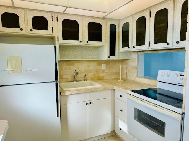 kitchen with white cabinetry, backsplash, white appliances, tile countertops, and sink