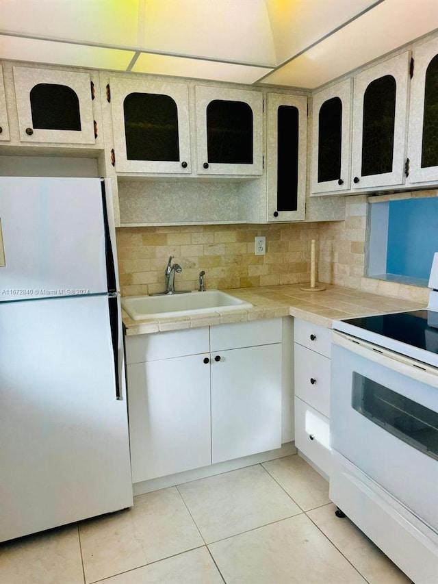 kitchen featuring white cabinets, light tile patterned floors, sink, white appliances, and tile counters