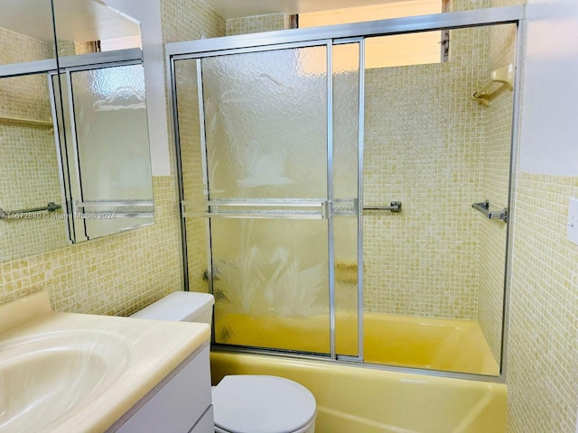full bath featuring toilet, tile walls, shower / bath combination with glass door, and vanity