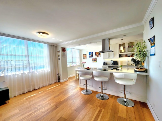 kitchen featuring island exhaust hood, crown molding, light hardwood / wood-style floors, and a kitchen bar