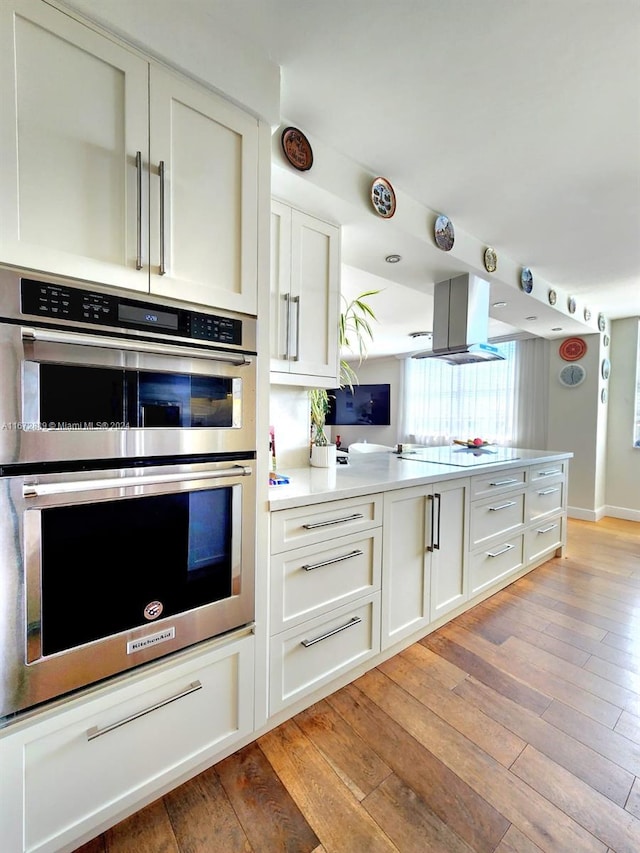 kitchen with light wood-type flooring, white cabinets, double oven, and island exhaust hood