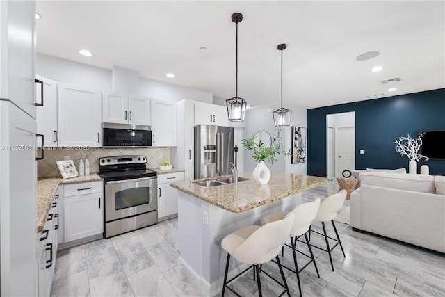 kitchen featuring an island with sink, appliances with stainless steel finishes, white cabinets, and decorative light fixtures