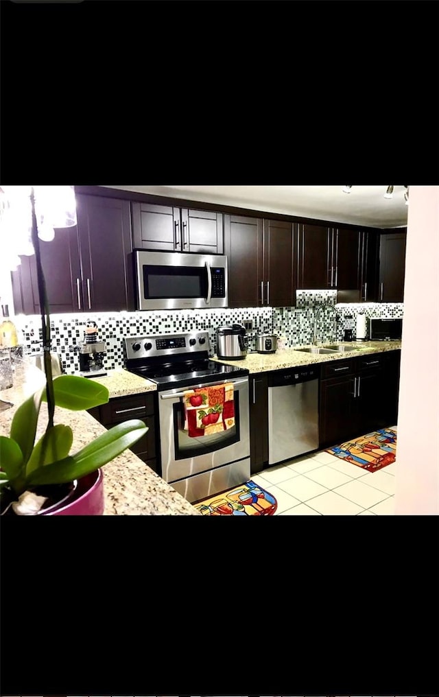 kitchen featuring decorative backsplash, dark brown cabinets, appliances with stainless steel finishes, and light tile patterned flooring