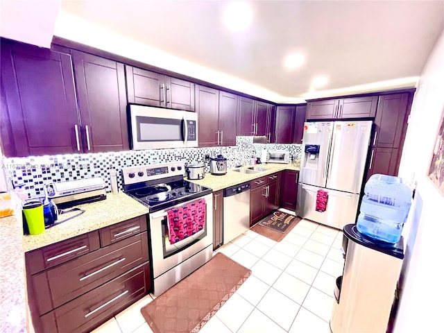 kitchen with light tile patterned floors, sink, stainless steel appliances, light stone countertops, and decorative backsplash