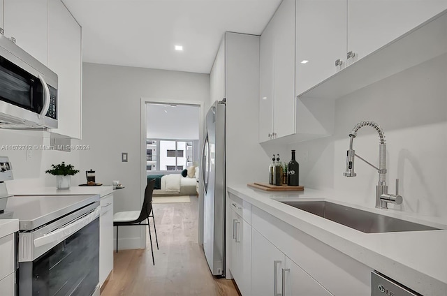 kitchen featuring sink, stainless steel appliances, light hardwood / wood-style floors, and white cabinetry