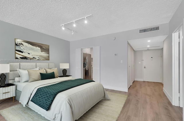 bedroom with stainless steel fridge, light hardwood / wood-style floors, and a textured ceiling