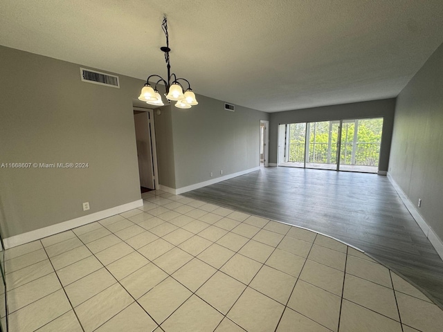 empty room featuring an inviting chandelier, light hardwood / wood-style floors, and a textured ceiling