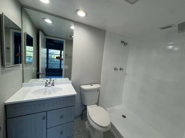 bathroom with a tile shower, vanity, tile patterned flooring, and toilet