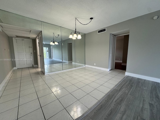 empty room with a notable chandelier, a textured ceiling, and light tile patterned floors