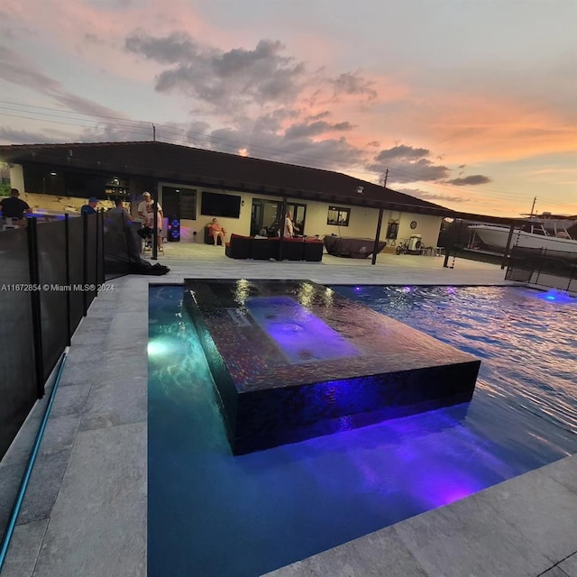 pool at dusk featuring outdoor lounge area, a patio, and an in ground hot tub