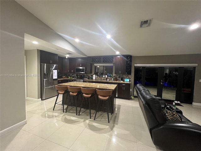 kitchen with appliances with stainless steel finishes, light tile patterned floors, a kitchen bar, and a kitchen island