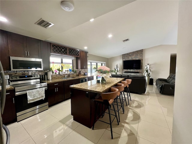 kitchen featuring appliances with stainless steel finishes, a center island, a breakfast bar area, vaulted ceiling, and light tile patterned floors