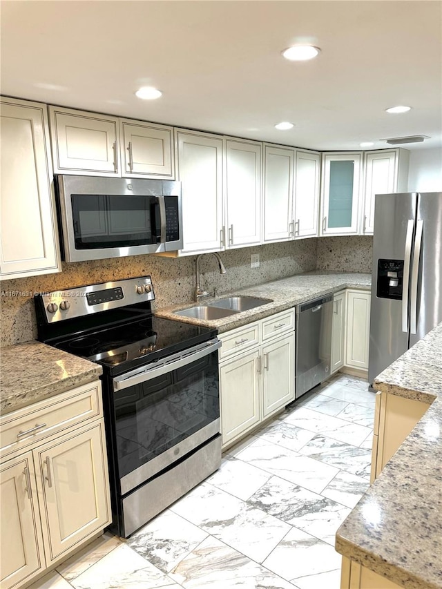 kitchen with light stone countertops, stainless steel appliances, cream cabinetry, and sink