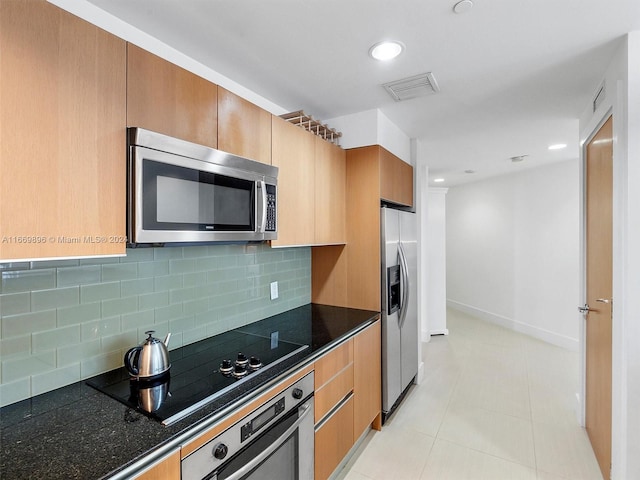 kitchen with dark stone countertops, appliances with stainless steel finishes, light tile patterned floors, and tasteful backsplash