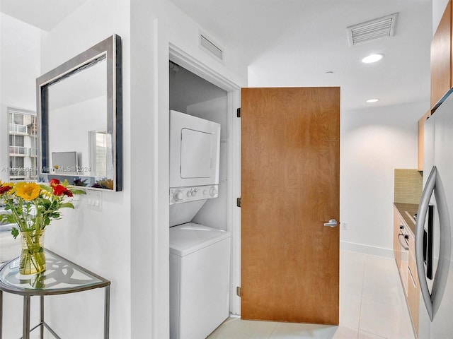 laundry area with stacked washer and dryer and light tile patterned floors