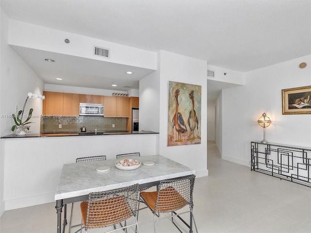 kitchen with appliances with stainless steel finishes, backsplash, kitchen peninsula, a breakfast bar area, and light brown cabinetry