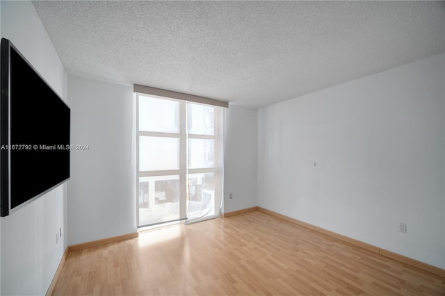 spare room featuring floor to ceiling windows, a textured ceiling, and light hardwood / wood-style flooring