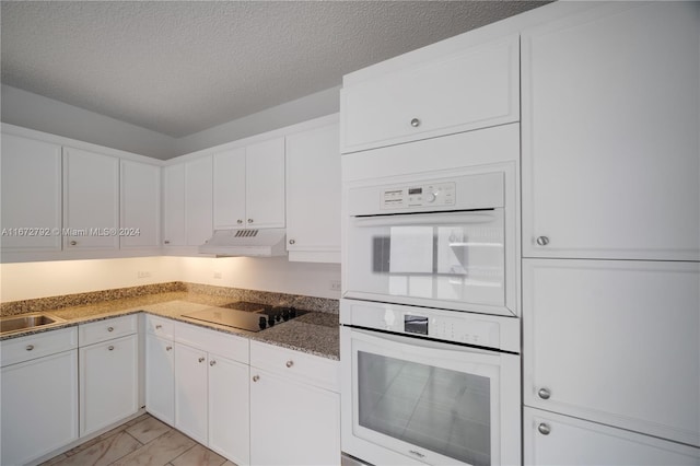 8855 Collins Ave Unit 2D, Surfside, FL 33154 - kitchen with black electric stovetop, under cabinet range hood, white double oven, white cabinetry, and a textured ceiling