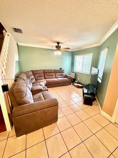 tiled living room with ceiling fan, a textured ceiling, and crown molding